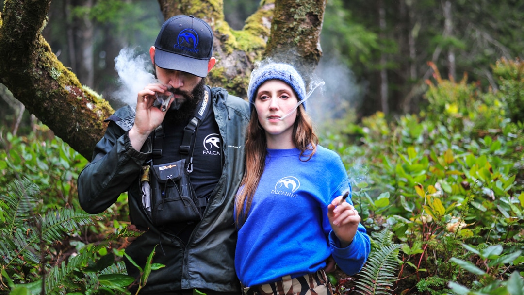 Falcanna founders Bethany and Justin Rondeaux, decked out in Falcanna gear, smoke joints in the woods.
