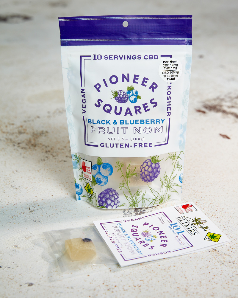 A 10-pack of high-CBD Black and Blueberry Pioneer Squares sits on a granite surface. A single serving sits in the foreground.
