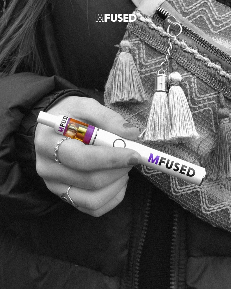 A black and white portrait of a hand holding a full-color Mfused vape battery topped with an Mfused cartridge.